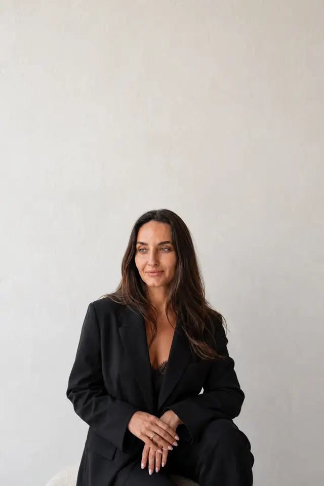 Kellen seated in a black suit against a white wall